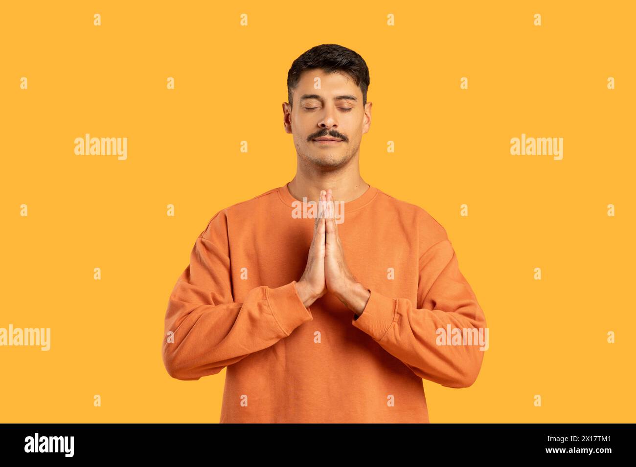 Mann mit Schnurrbart in Gebetsposition auf Orange Stockfoto