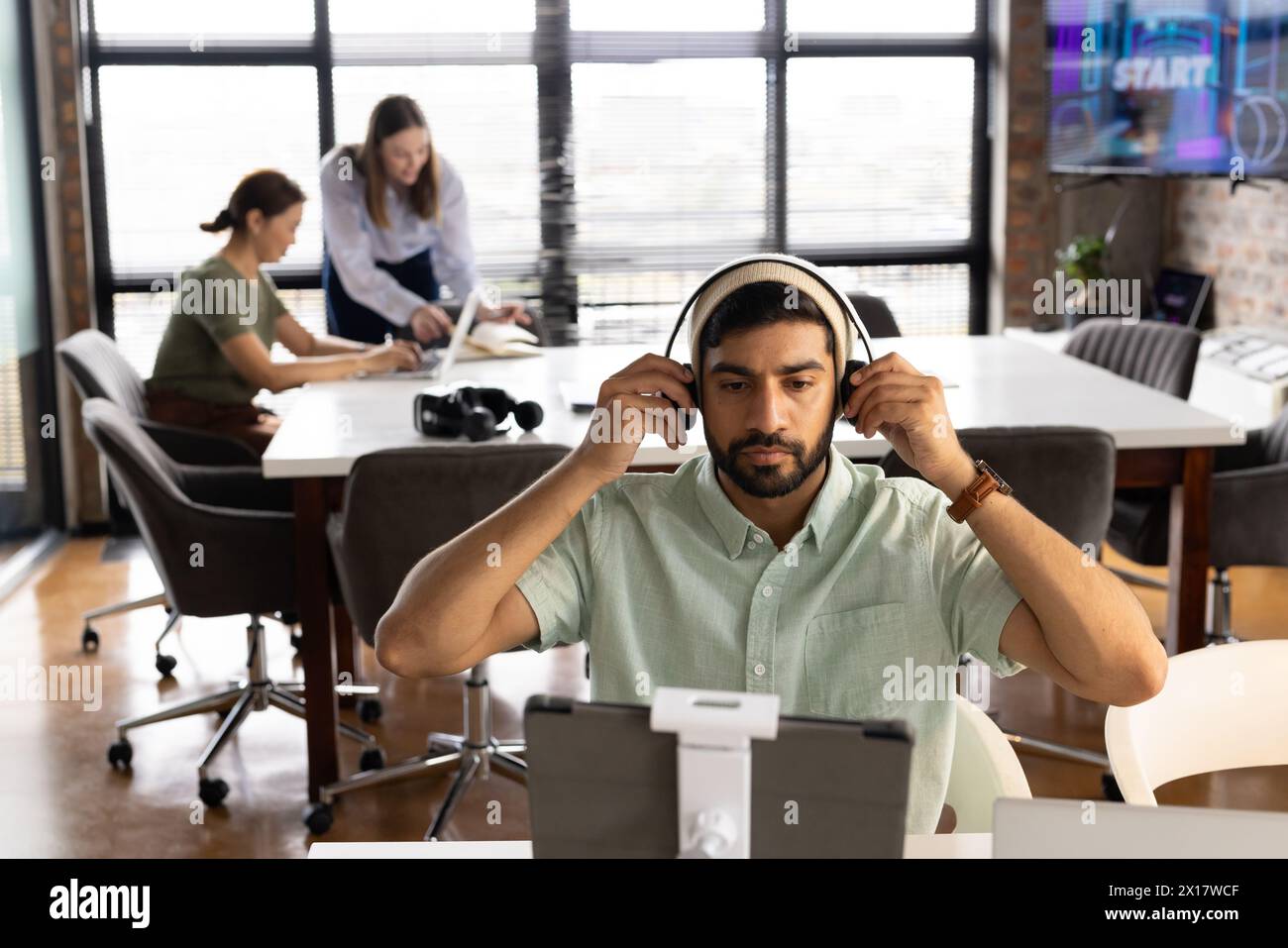 Ein vielseitiges Team arbeitet in einem modernen Geschäftsbüro, wobei ein junger asiatischer Mann sich auf einen Computer konzentriert Stockfoto