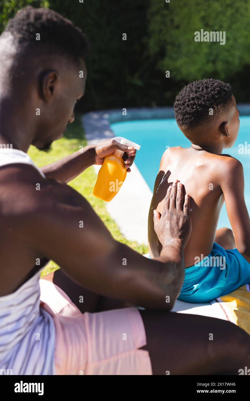 Ein afroamerikanischer Vater, der seinen Sohn am Pool zu Hause mit Sonnencreme behandelt Stockfoto