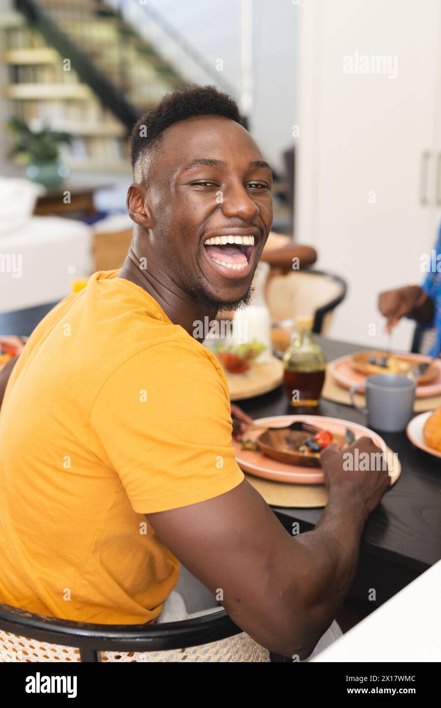Afroamerikaner lacht beim Familienfrühstück zu Hause, Frau greift nach Essen Stockfoto