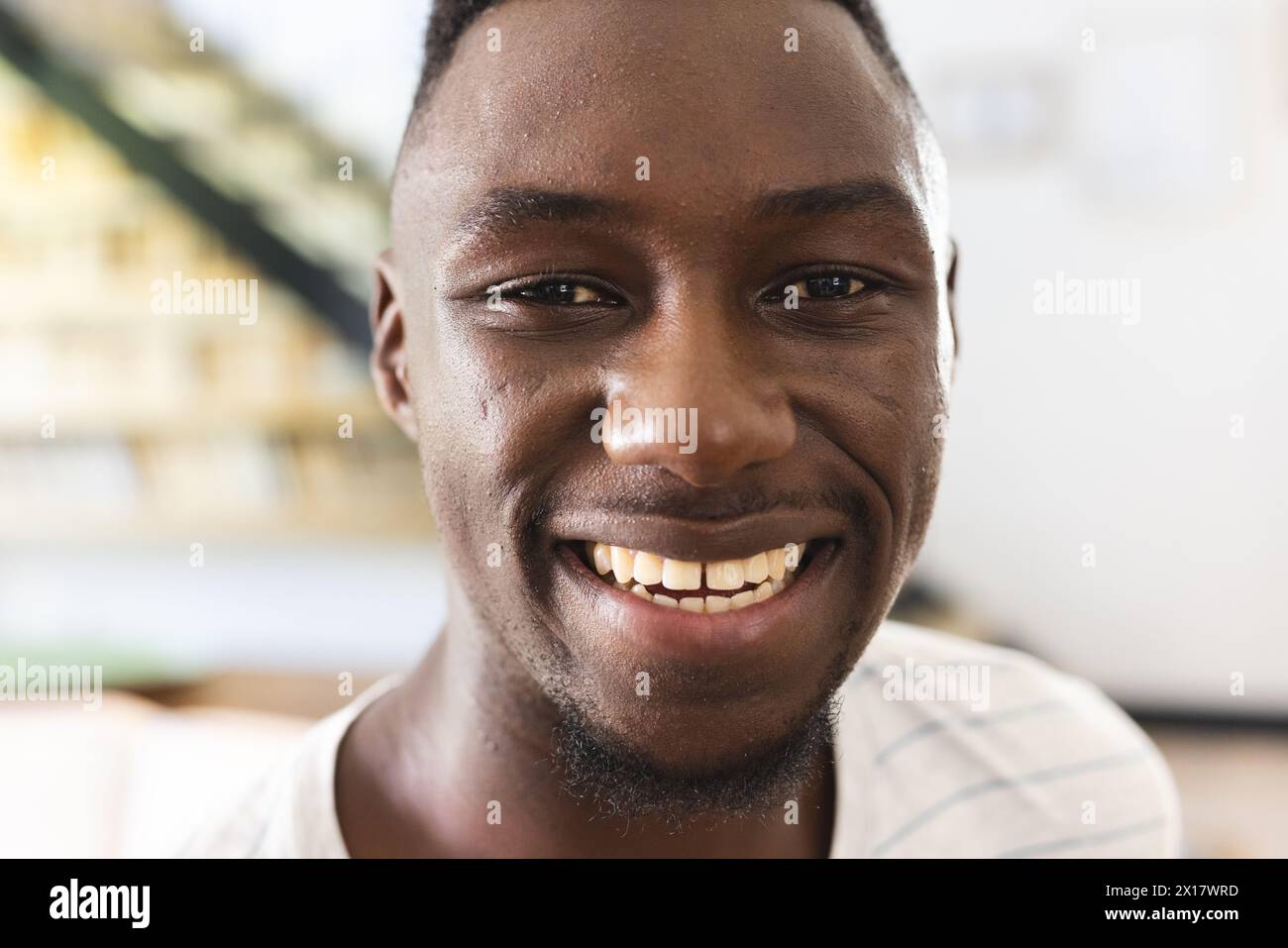Ein junger Afroamerikaner mit einem hellen Lächeln, der zu Hause ein kariertes Hemd trägt Stockfoto