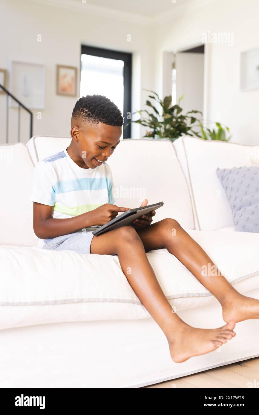 Afroamerikaner sitzt auf der Couch und konzentriert sich auf eine Tablette Stockfoto