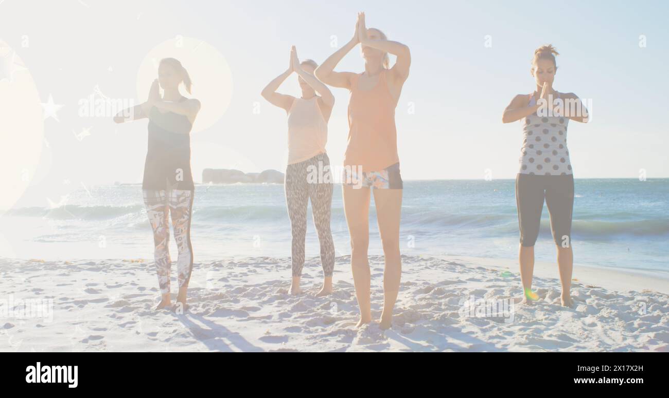 Bild von leuchtenden Lichtern über einer Gruppe verschiedener weiblicher Freunde, die Yoga am Meer ausüben Stockfoto