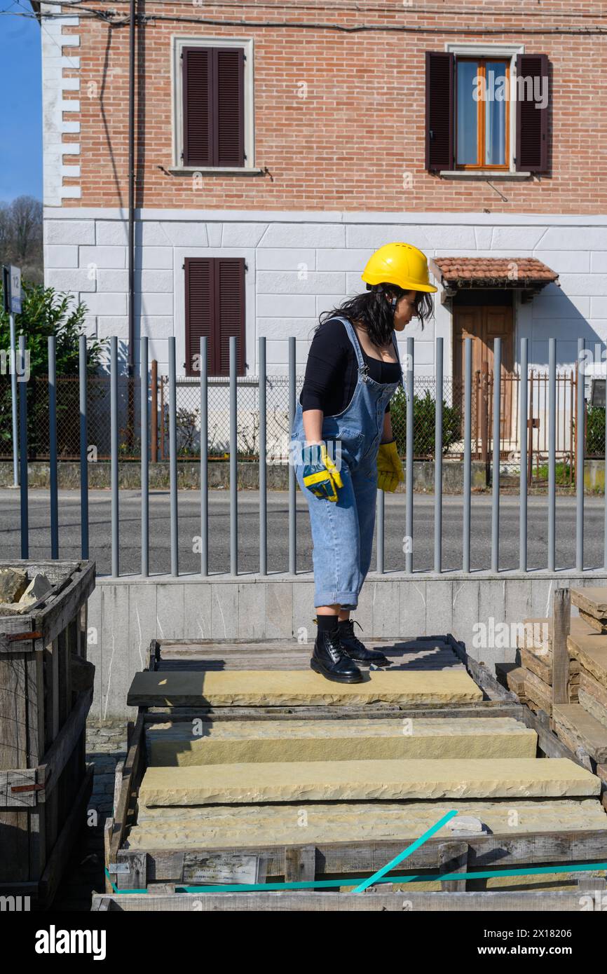 Eine Frau in Bauausrüstung steht an einem Zaun und misst etwas auf einer Baustelle Stockfoto