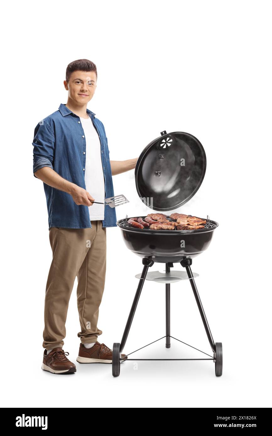 Junger Mann, der Fleisch auf einem Grill zubereitet und einen turner isoliert auf weißem Hintergrund hält Stockfoto