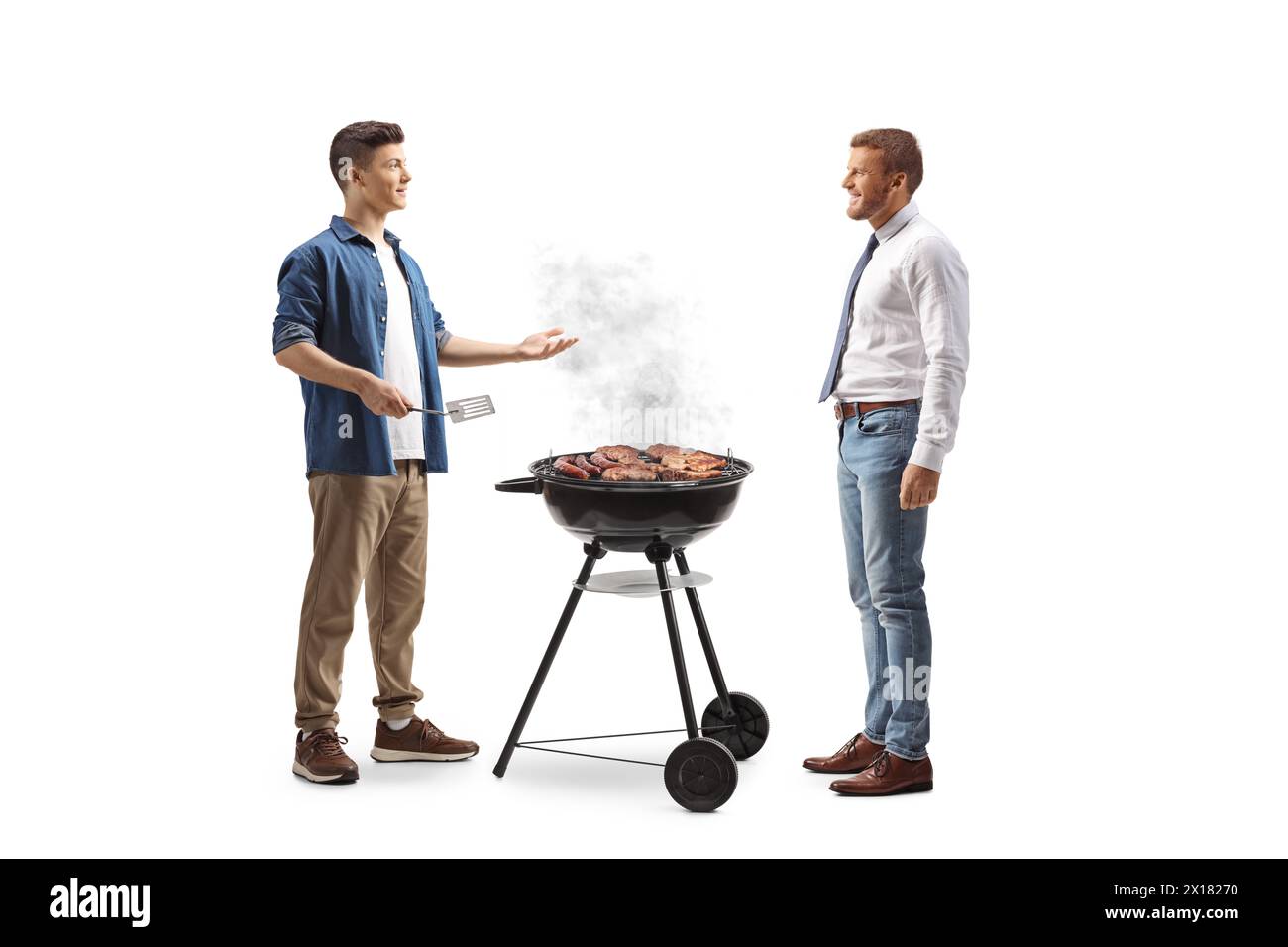 Junger Mann, der Fleisch auf einem Grill zubereitet und mit einem Freund auf weißem Hintergrund spricht Stockfoto