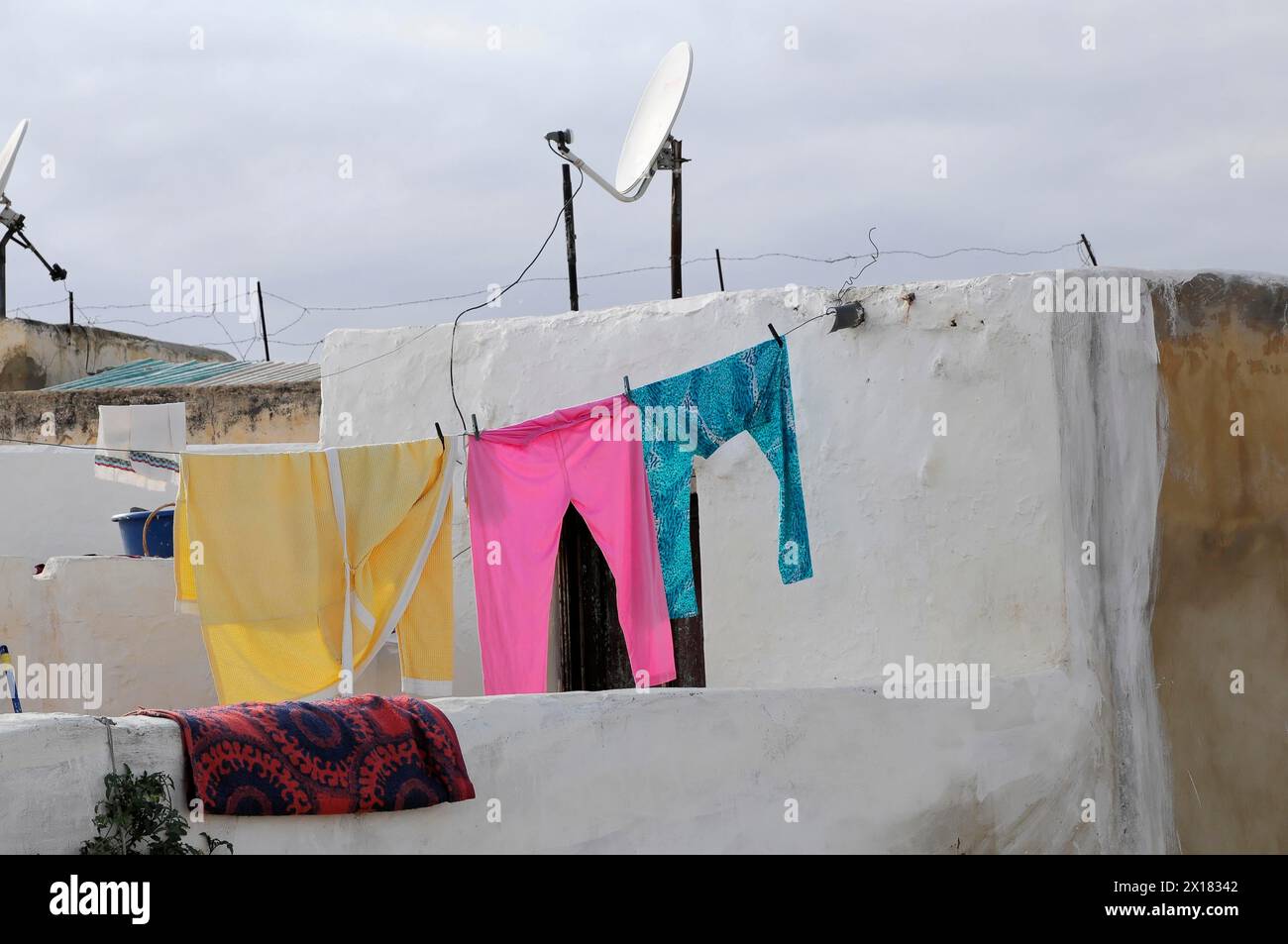 Meknes, farbenfrohe Wäsche hängt an einer Linie vor einer weißen Wand mit einer Satellitenschüssel im Hintergrund, Nordmarokko, Marokko Stockfoto