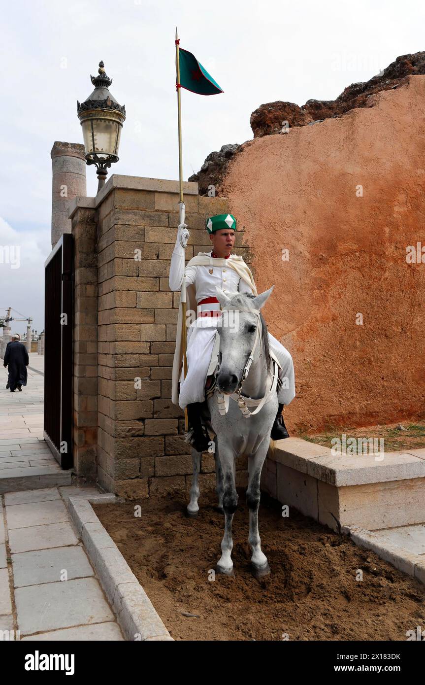 Berittener Wachsoldat in traditioneller Kleidung vor der unvollendeten Moschee, Rabat, Wachsoldat in Uniform, der auf einem weißen Pferd vor einem alten Pferd reitet Stockfoto