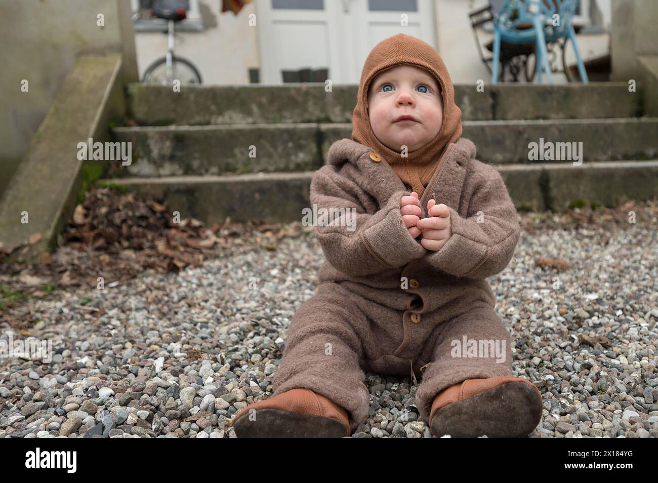 Kleines Kind, 8 Monate, warm eingewickelt, auf dem Kies sitzend und mit Steinen spielend, Mecklenburg-Vorpommern, Deutschland Stockfoto