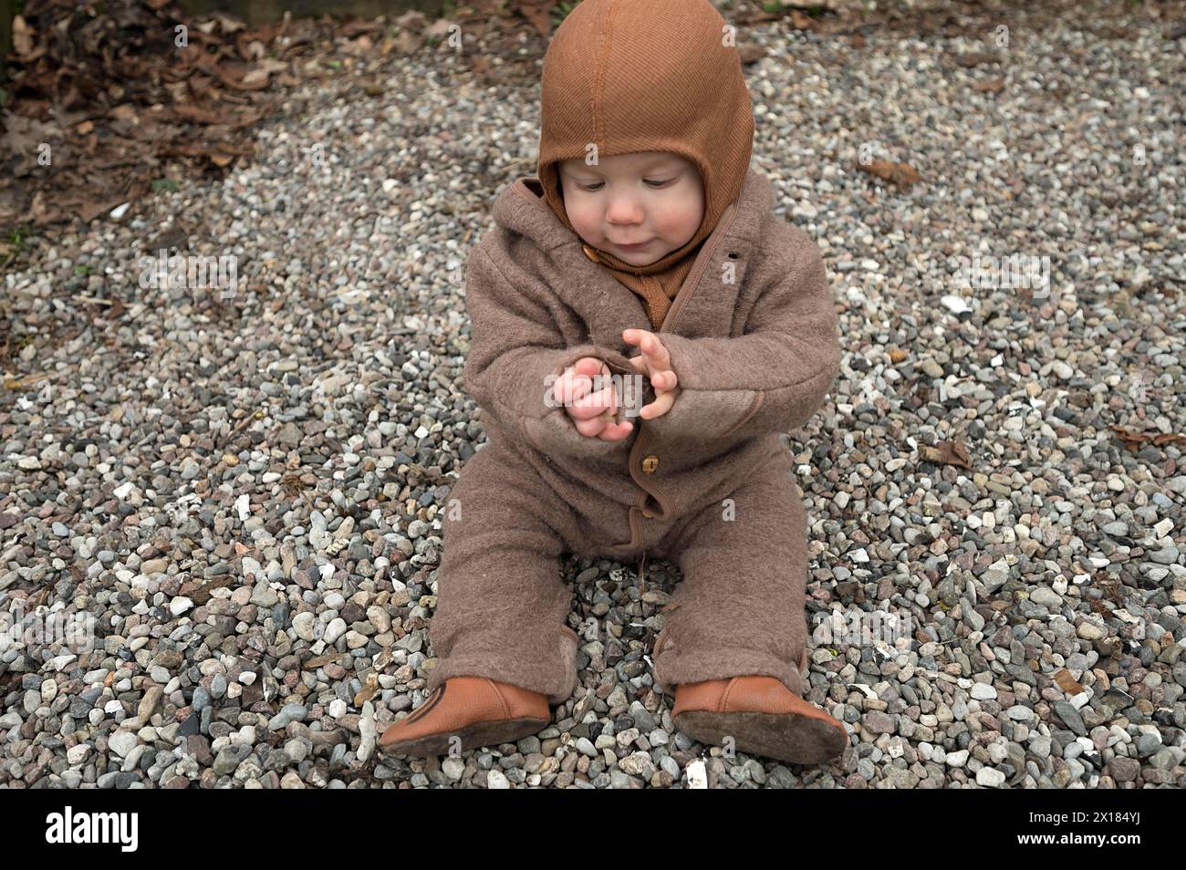 Kleines Kind, 8 Monate, warm eingewickelt, auf dem Kies sitzend und mit Steinen spielend, Mecklenburg-Vorpommern, Deutschland Stockfoto