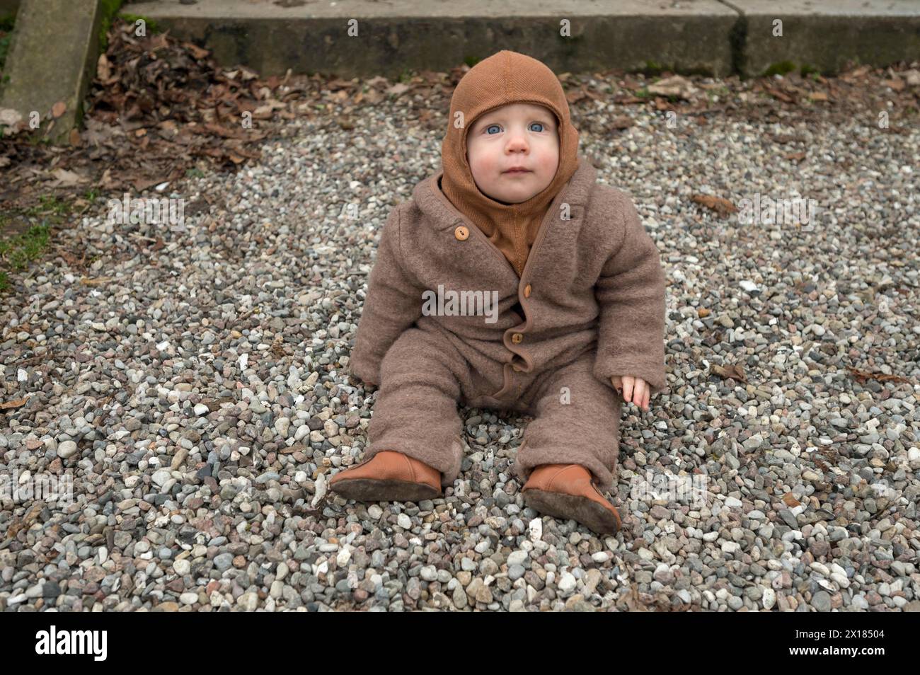 Kleines Kind, 8 Monate, warm eingewickelt, auf dem Kies sitzend, Mecklenburg-Vorpommern, Deutschland Stockfoto