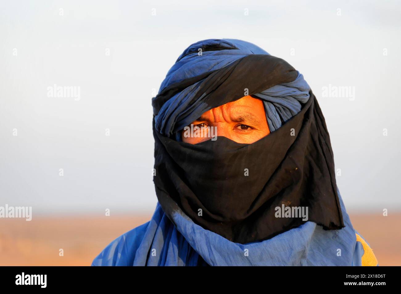 Sanddünen von Erg Chebbi, Erfoud, Meknes-Tafilalet, Porträt einer Person mit blauem Tuareg-Turban und Gesichtsbedeckung in der Abenddämmerung, Mittlerer Atlas, Marokko Stockfoto