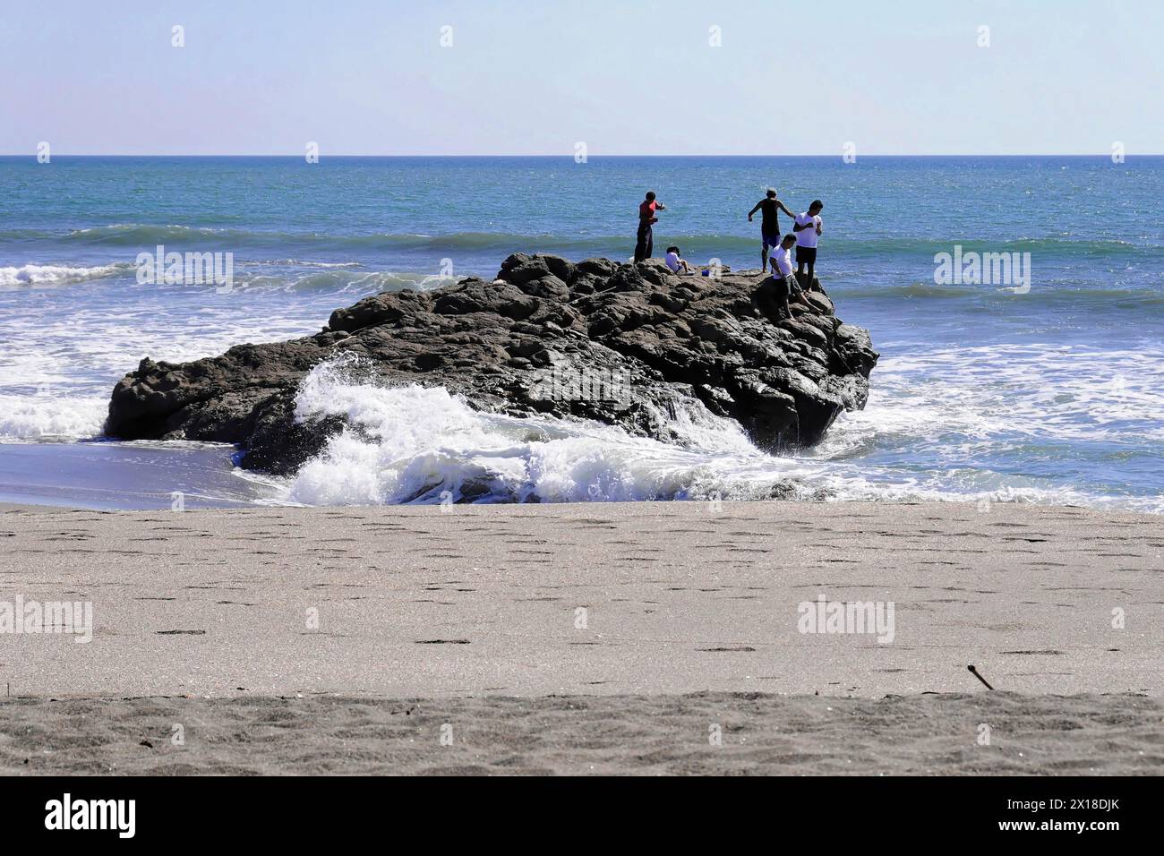 Las Penitas Strand in der Nähe von Poneloya, Leon, Pazifik, Nicaragua, Menschen auf einem Felsen am Strand mit brechenden Wellen, Mittelamerika, Mittelamerika Stockfoto