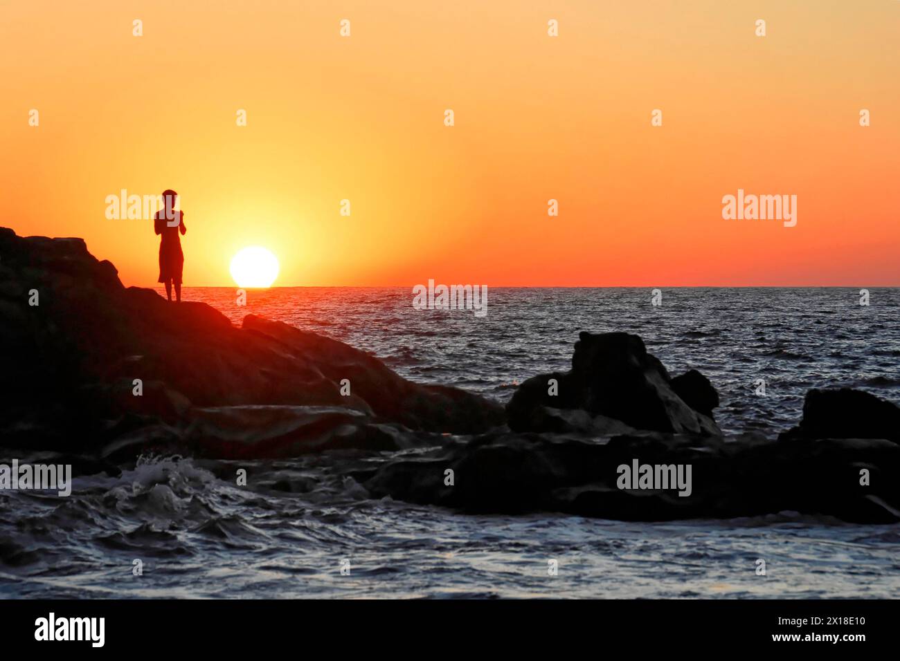 Strand in der Nähe von Poneloya, Las Penitas, Leon, Nicaragua, Frau Silhouetten auf einem Felsen, Meer mit Wellen bei Sonnenuntergang, Mittelamerika, Mittelamerika Stockfoto