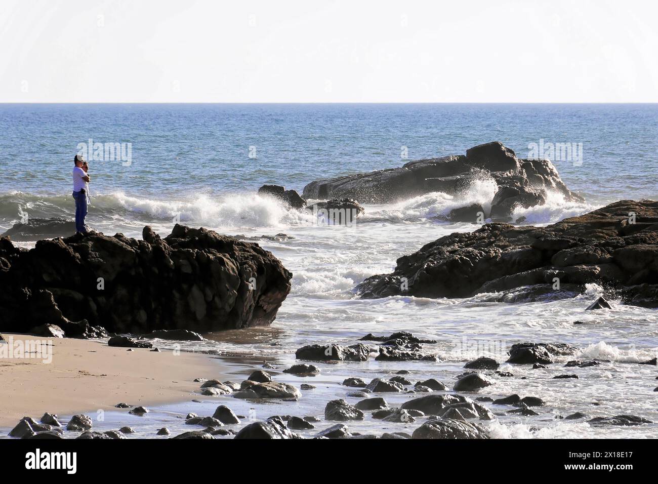 Strand in der Nähe von Poneloya, Las Penitas, Leon, Nicaragua, Eine Person steht auf Felsen am Meer und fotografiert die Wellen, Mittelamerika, Mittelamerika Stockfoto
