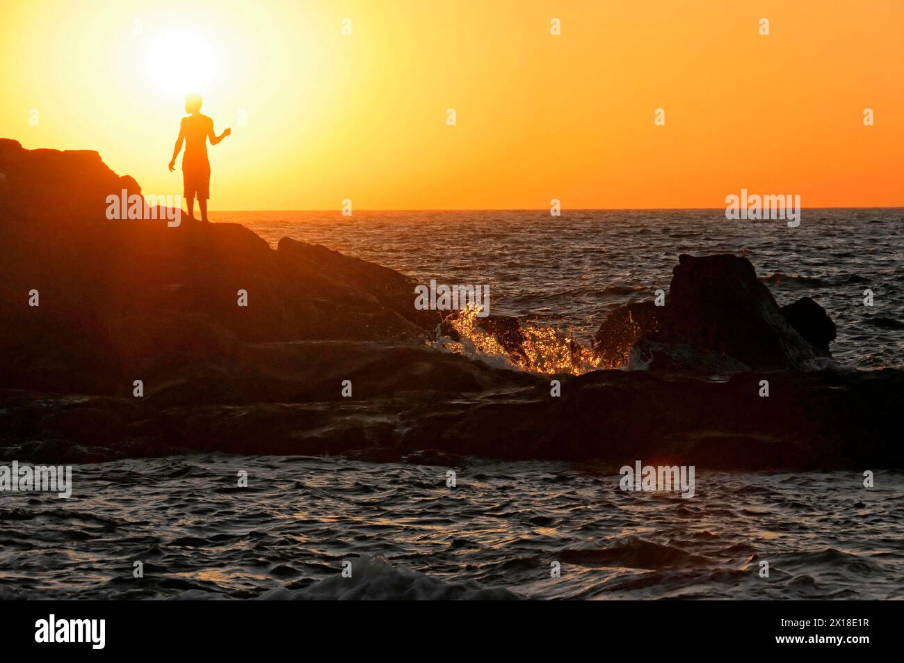 Strand in der Nähe von Poneloya, Las Penitas, Leon, Nicaragua, Silhouette einer Person am Meer auf Felsen, kleine Wellen brechen im Sonnenlicht, Mittelamerika Stockfoto