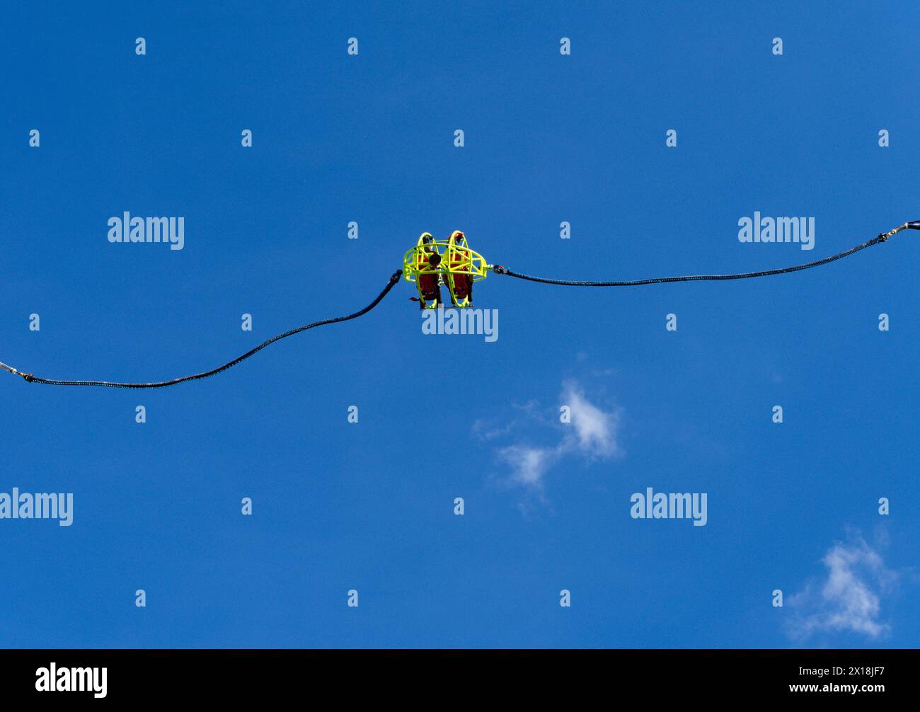 Zwei aufregende Freunde in einer gelben Schlinge schweben hoch in einen blauen Himmel mit Wolken. Auf einem Spielplatz während eines Frühlingstages in Italien. Stockfoto