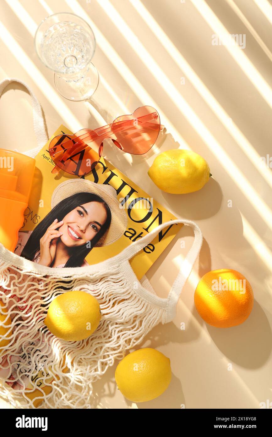 Schnur Tasche mit frischem Obst, Modemagazin und Strandaccessoires auf beigefarbenem Hintergrund, flache Lay Stockfoto