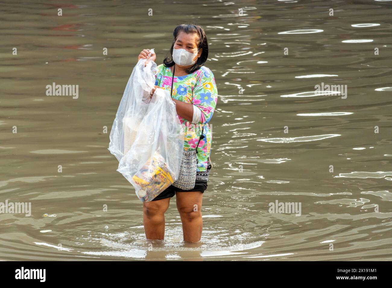 SAMUT PRAKAN, THAILAND, 11. Februar 2024, Eine Frau mit Plastiktüte waten durch eine überflutete Straße Stockfoto