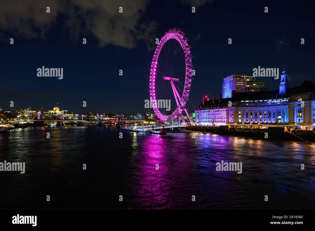 London, Großbritannien - 24. März 2024; Millennium Wheel oder London Eye drehen sich bei Nacht rosa über der Themse mit Reflexion Stockfoto