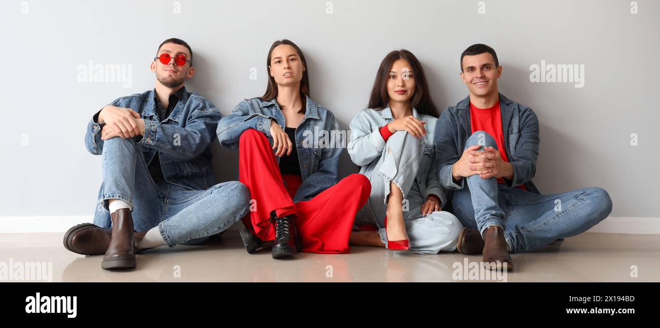 Gruppe junger Leute in stilvoller Denim-Kleidung, die in der Nähe einer hellen Wand sitzen Stockfoto