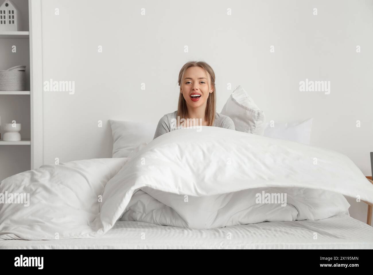 Glückliche junge Frau, die auf einem bequemen Bett im Schlafzimmer sitzt Stockfoto