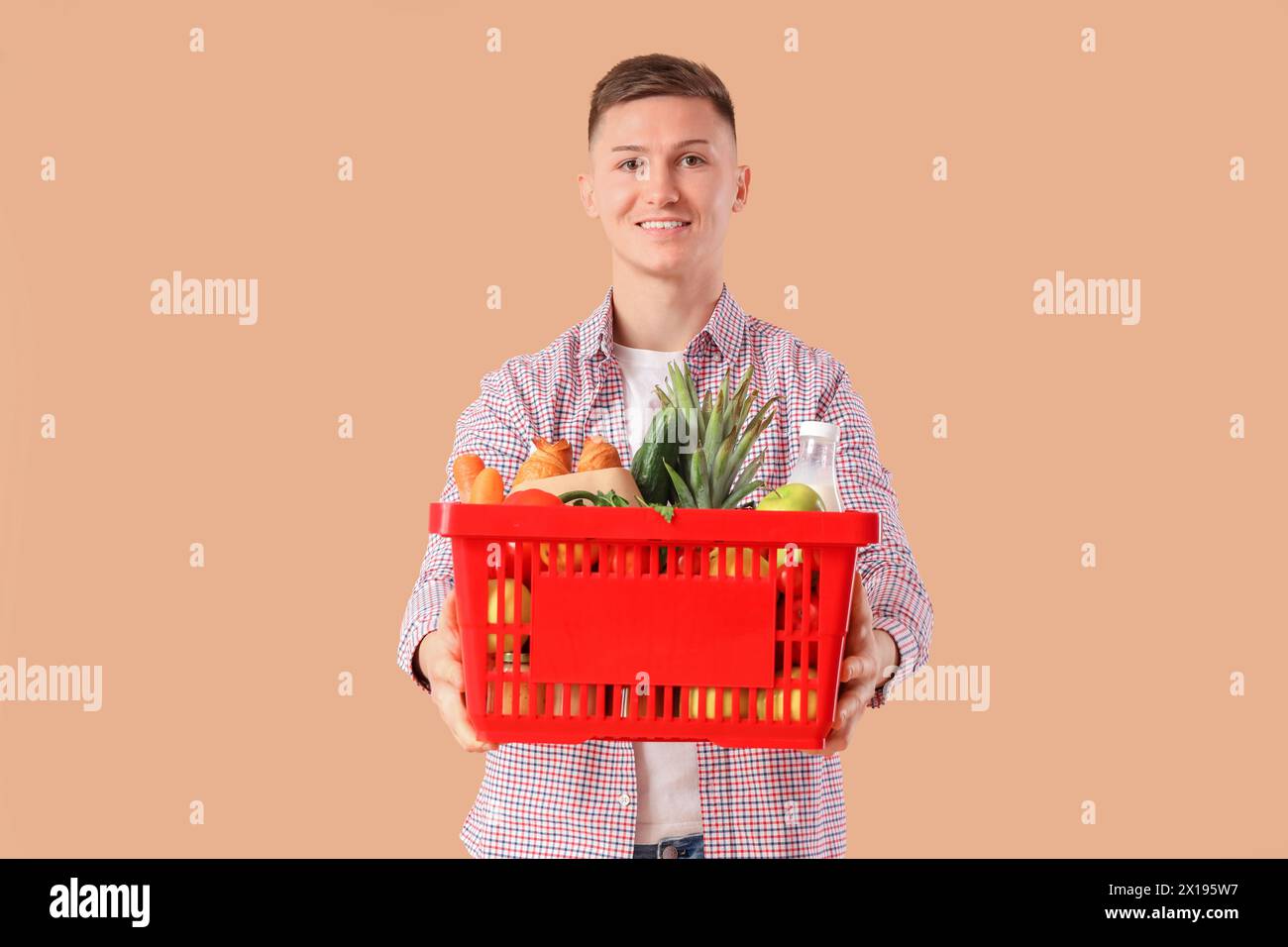 Junger Mann mit vollem Warenkorb auf beigefarbenem Hintergrund Stockfoto