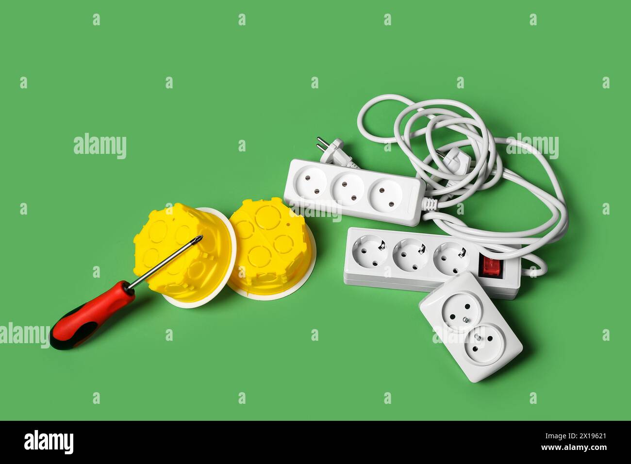 Verlängerungskabel, elektrische Anschlusskästen und Schraubendreher auf grünem Hintergrund Stockfoto