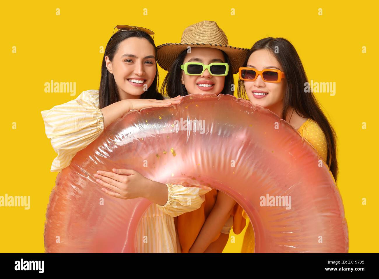 Schöne junge Frauen mit aufblasbarem Ring auf gelbem Hintergrund. Sommerparty Stockfoto