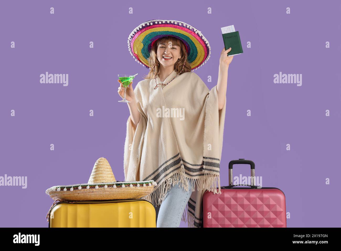 Wunderschöner junger glücklicher weiblicher Tourist in Sombrero Hut mit Koffern, Pass und Cocktail auf lila Hintergrund Stockfoto