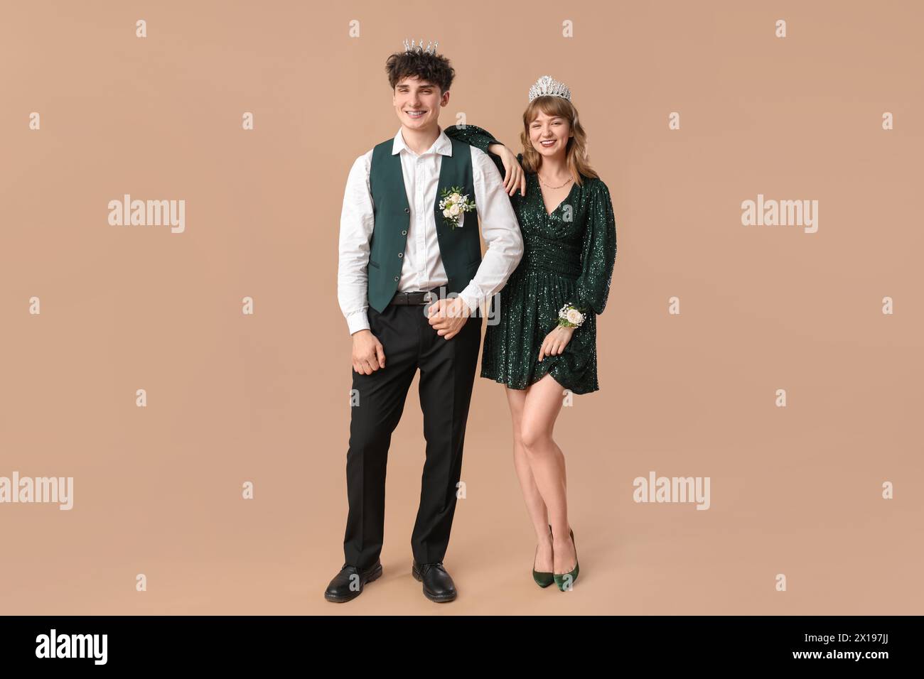 Glückliches Abschlussball-Paar mit Kronen auf beigefarbenem Hintergrund Stockfoto