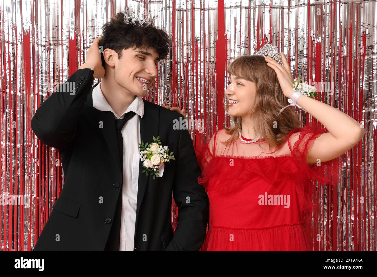 Glückliches Abschlussball-Paar in Kronen mit Lametta auf rotem Hintergrund Stockfoto