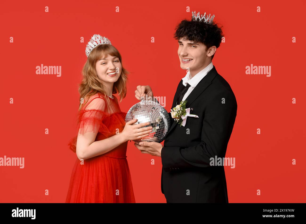 Glückliches Abschlussball-Paar in Kronen mit Discoball auf rotem Hintergrund Stockfoto