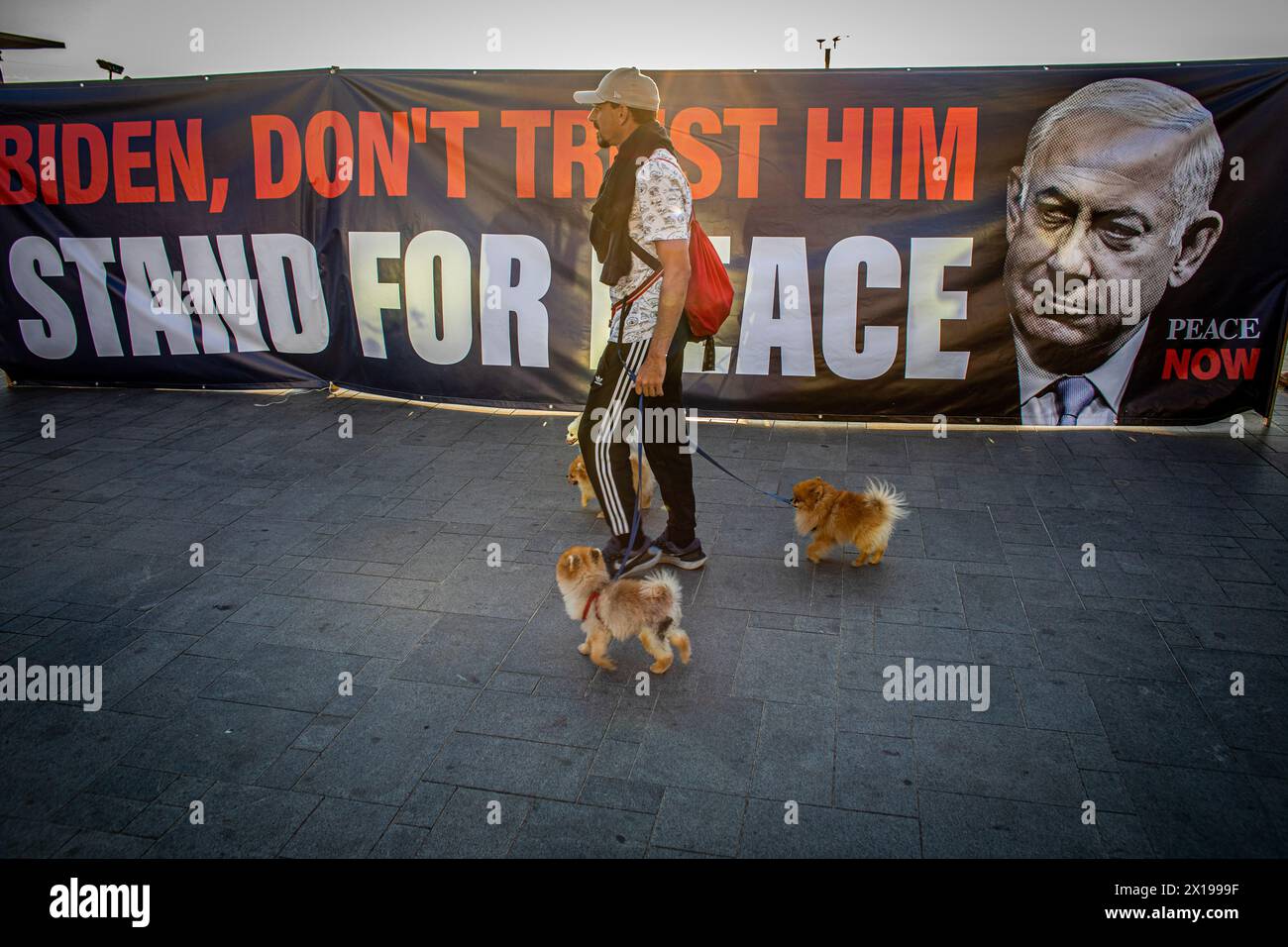 Tel Aviv, Israel. April 2024. Ein Mann geht mit seinen Hunden an einem Banner vorbei, das US-Präsident Joe Biden aufruft, den israelischen Premierminister Benjamin Netanjahu während einer Demonstration daran zu hindern, den Iran anzugreifen. Israel hat nach einem beispiellosen Drohnen- und Raketenangriff am Wochenende, der die regionalen Spannungen, die durch den Krieg in Gaza geschürt wurden, verschärft hat, gelobt, vom Iran einen "Preis" abzugeben. (Foto von Eyal Warshavsky/ SOPA Images/SIPA USA) Credit: SIPA US/Alamy Live News Stockfoto