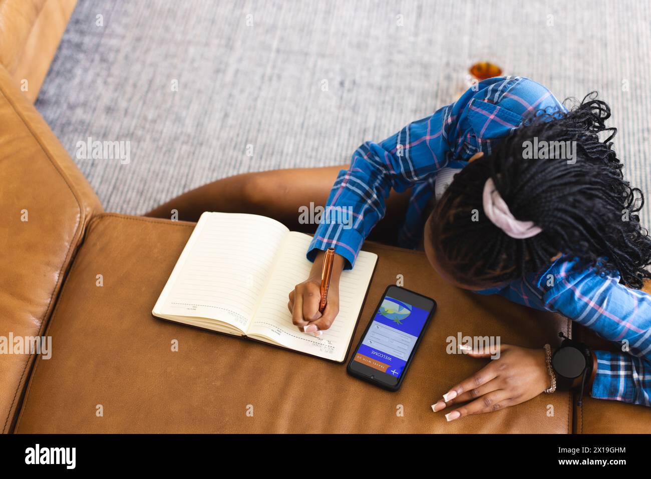 Afroamerikanische junge Frau mit blauem kariertem Hemd, die zu Hause im Notizbuch mit Kopierraum schreibt Stockfoto