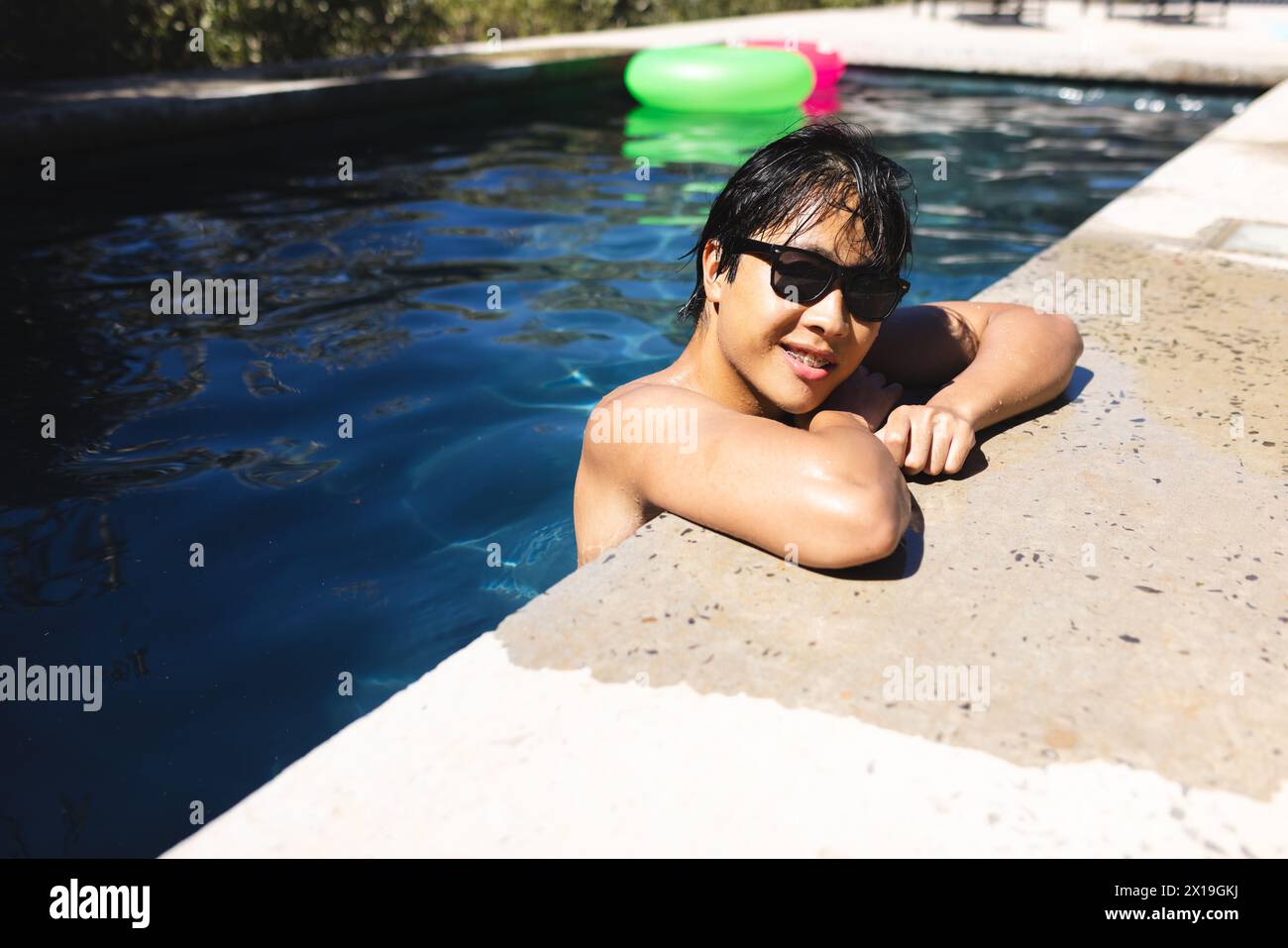 Ein Teenager asiatischer Junge, der sich zu Hause im Pool entspannt, Sonnenbrille trägt, Kopierraum Stockfoto