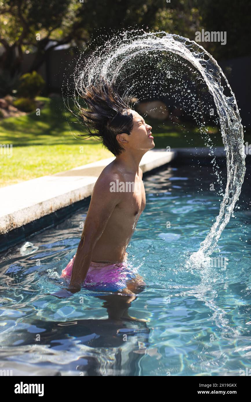 Der Teenager Asiatische Junge dreht sich draußen im Pool die Haare und erzeugt einen Wasserbogen Stockfoto