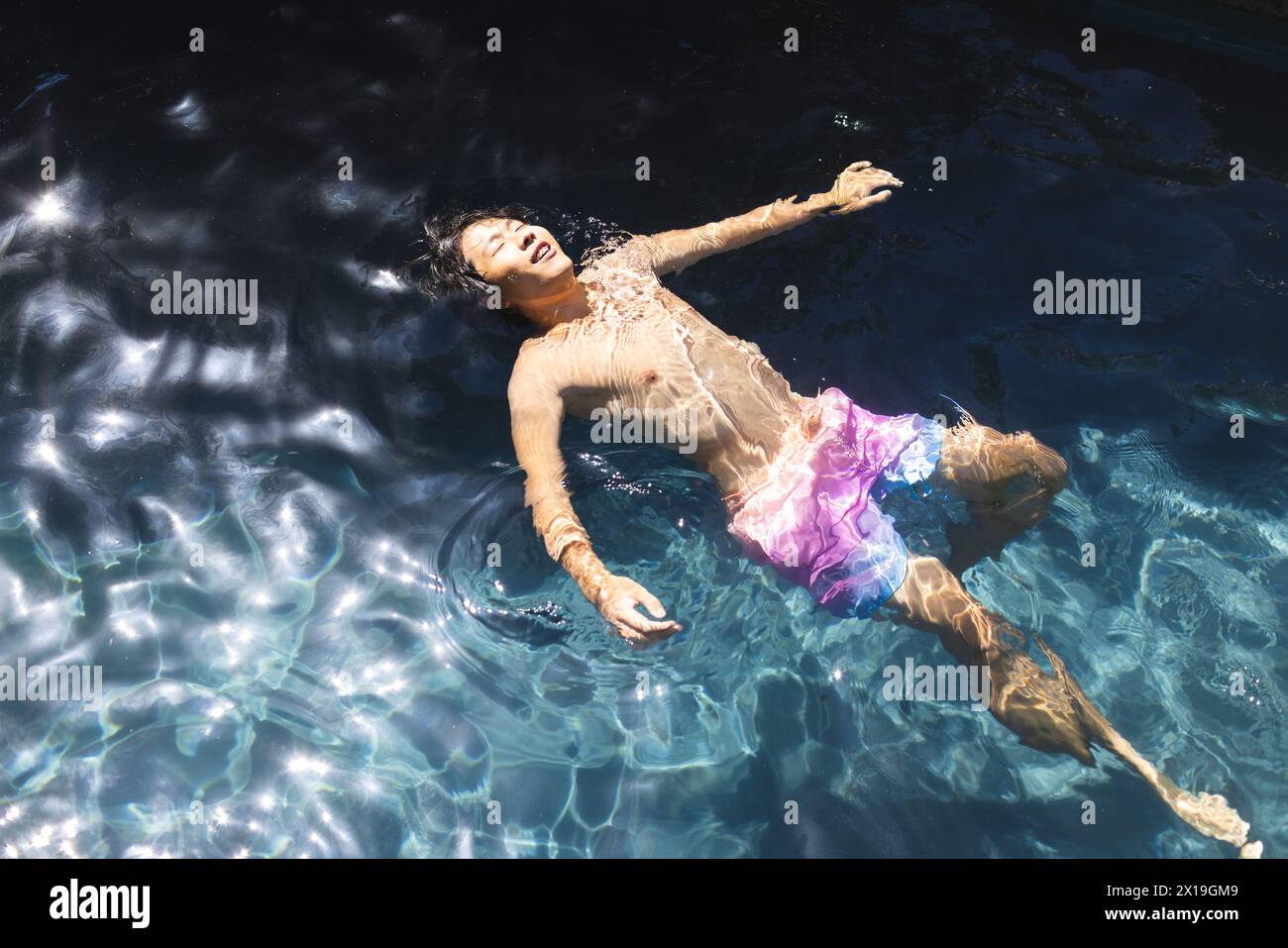 Ein asiatischer Teenager schwimmt draußen in einem Pool, trägt einen rosa Schwimmboden, Kopierraum Stockfoto
