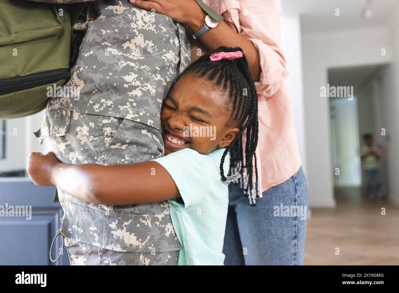 Ein junges afroamerikanisches Mädchen mit geflochtenen Haaren, das den Soldaten zu Hause umarmt und Liebe zeigt Stockfoto