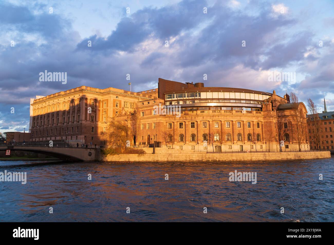 Das schwedische parlamentsgebäude in Stockholm bei Sonnenuntergang, Orangetöne, bewölkter Himmel, der Fluss Norrström im Vordergrund. Stockfoto