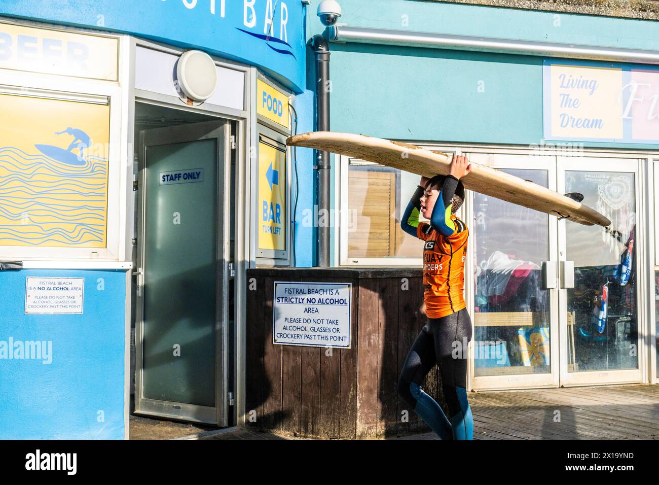 Ein junger männlicher Surfer, der sein Surfbrett auf dem Kopf balanciert und nach einer Surfsession in Newquay in Cornwall in Großbritannien nach Hause geht. Stockfoto