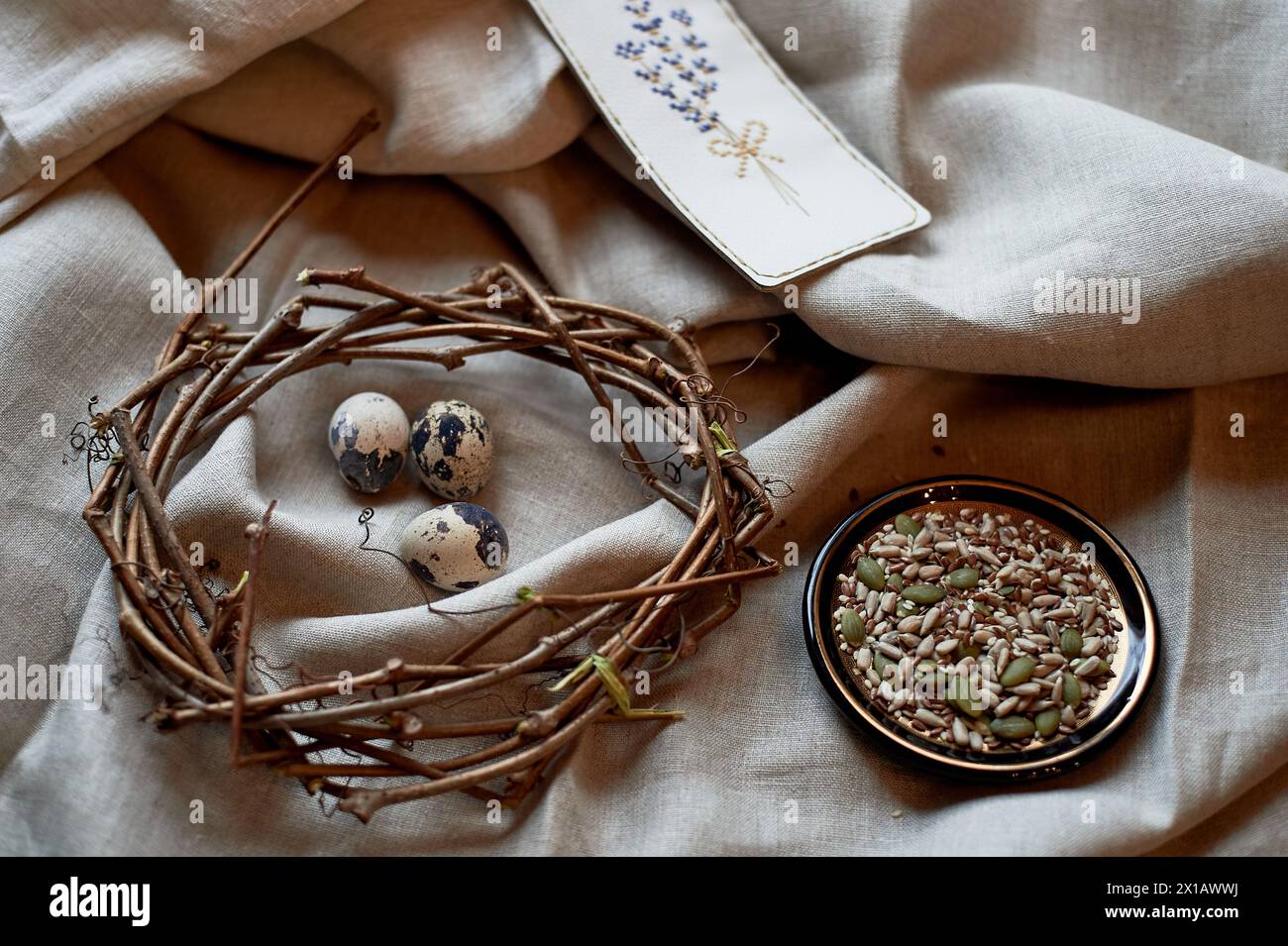 Ein Kranz aus Wachteleiern, wunderschön auf einem hölzernen Serviergeschirr ausgestellt, begleitet von einem Teller mit verschiedenen Samen. Das Arrangement ist mit twi verziert Stockfoto
