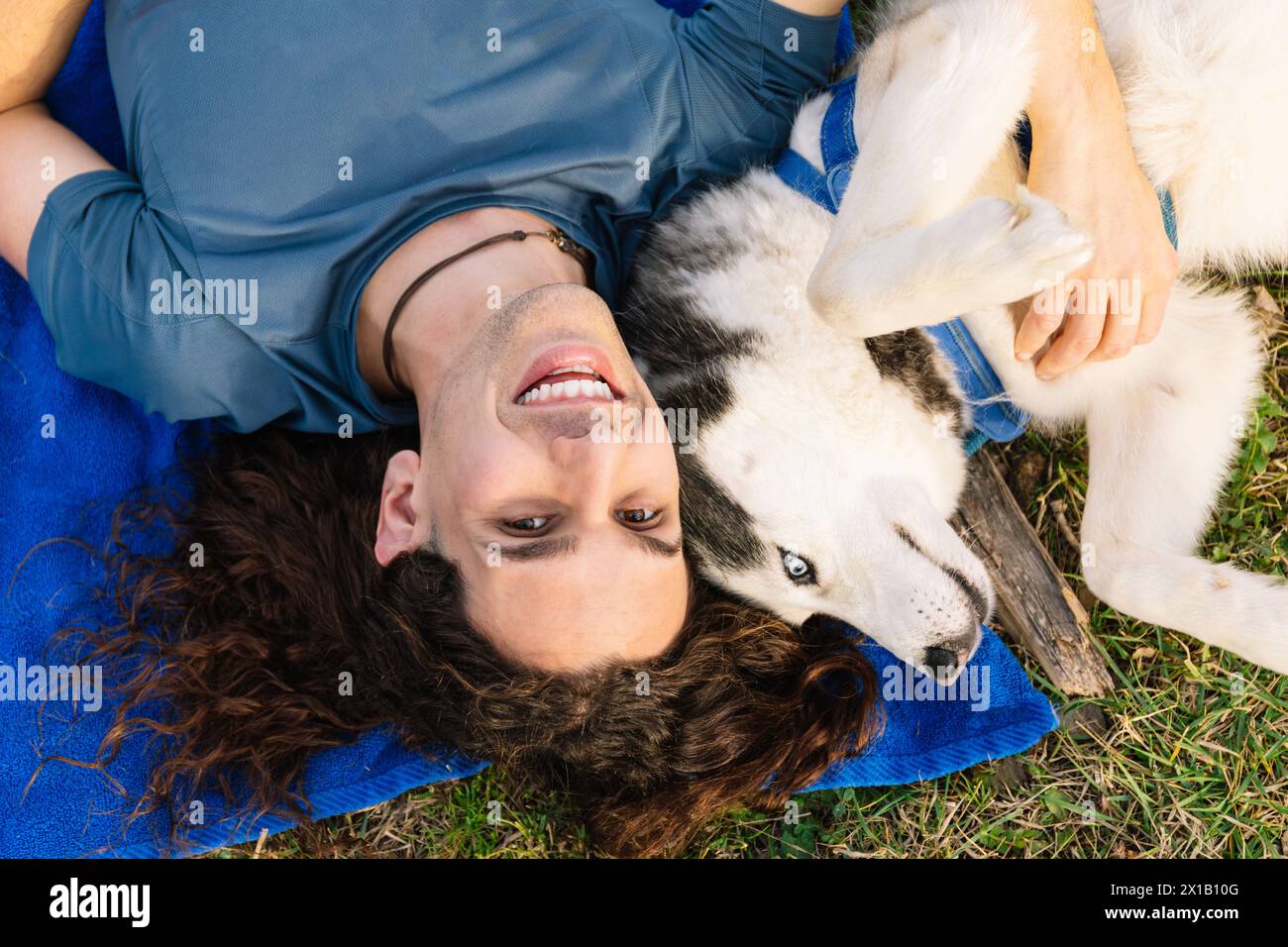 Horizontales Foto ein Mann und sein Husky liegen spielerisch kopfüber auf dem Gras und teilen eine einzigartige Perspektive und eine fröhliche Verbindung im gre Stockfoto