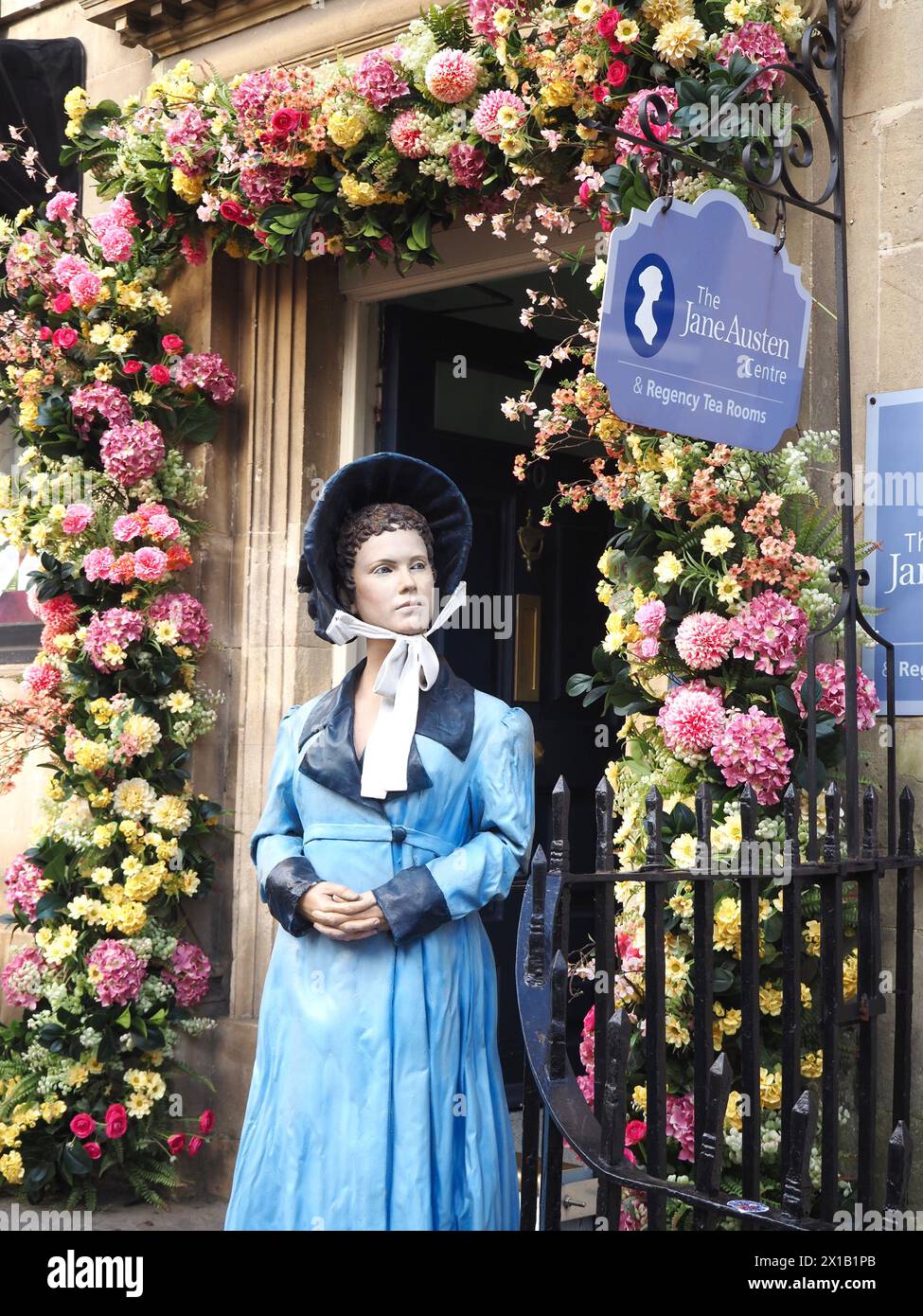 Eintritt zum Jane Austen Centre mit dem Modell von Jane Austen in georgianischer Kleidung, eingerahmt von Blumengirlanden rund um die georgianische Steintür Stockfoto