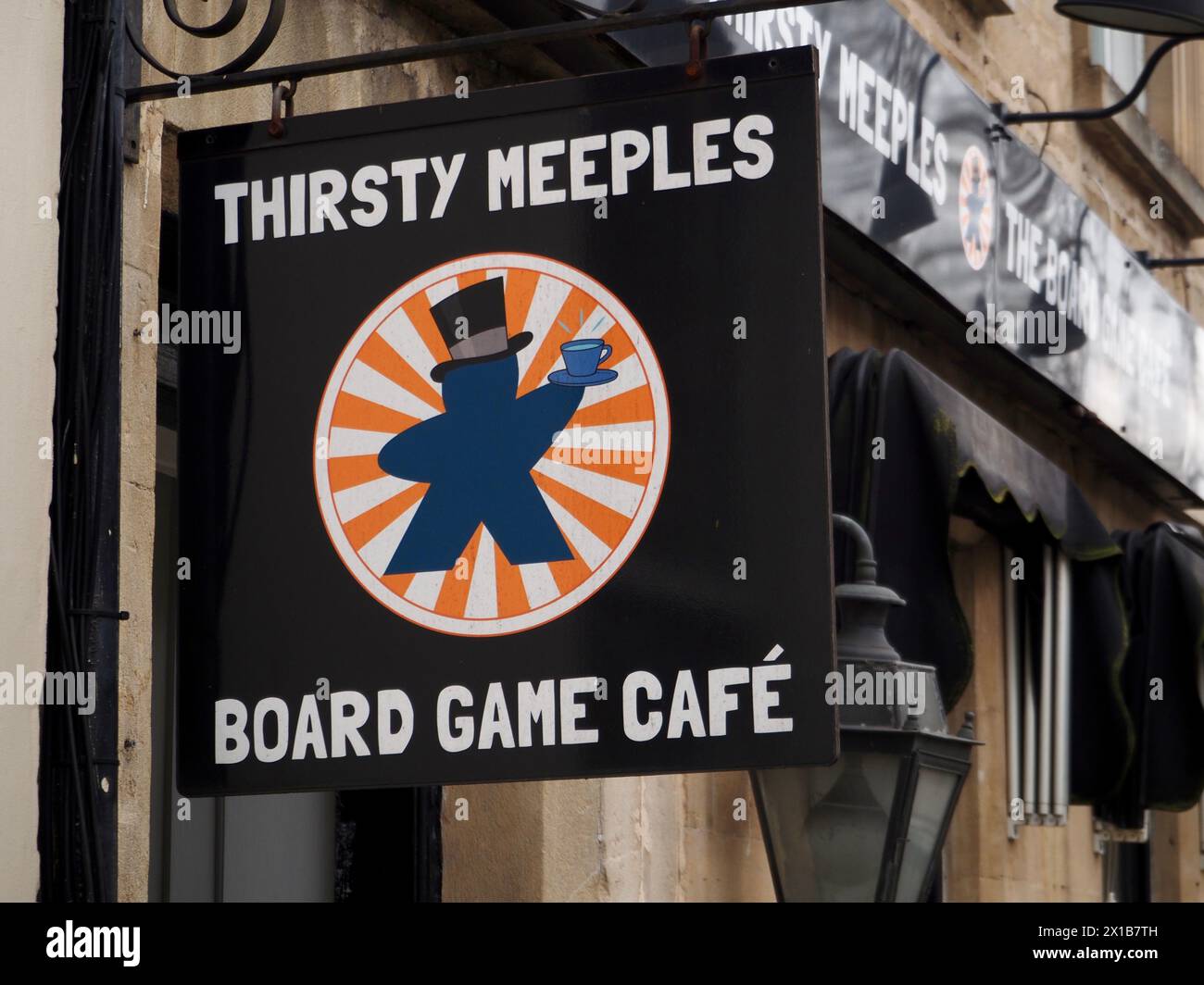 Hängende Schildertafel über dem Eingang zu Thirsty Meeples, einem Café in Gay Street Bath, das sich an Brettspiel-Enthusiasten richtet. Das Schild zeigt ein meeple-Spielstück Stockfoto