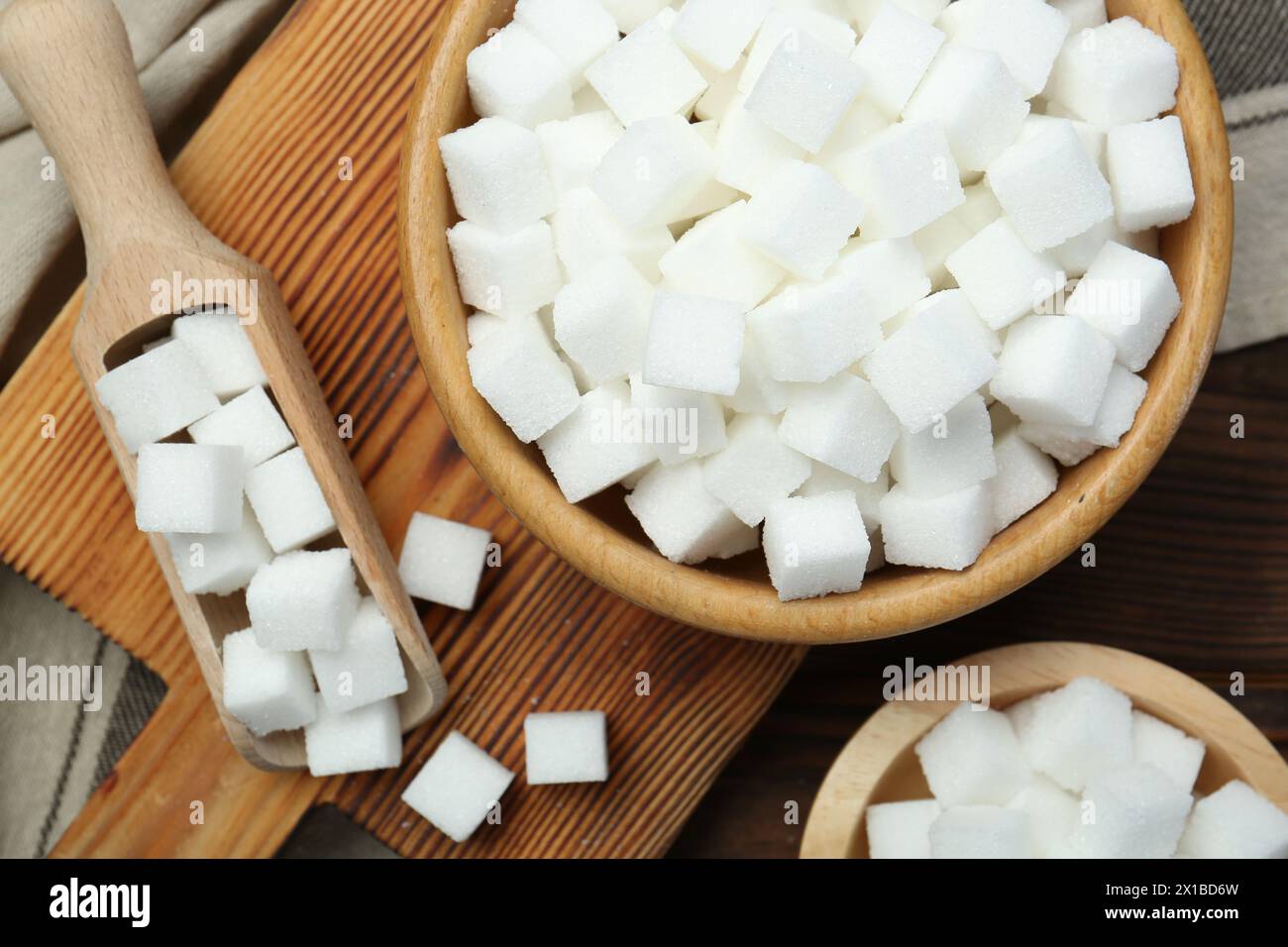 Weiße Zuckerwürfel in Schüsseln und Löffel auf Holztisch, flach gelegt Stockfoto