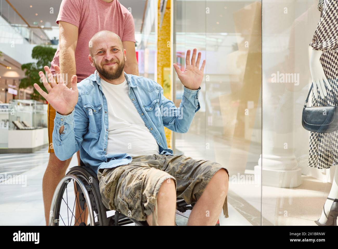 Ein freundlicher Mann im Rollstuhl begrüßt mit einem Lächeln beim Einkaufen in einem Einkaufszentrum und hebt unabhängiges Leben und Inklusivität hervor. Stockfoto