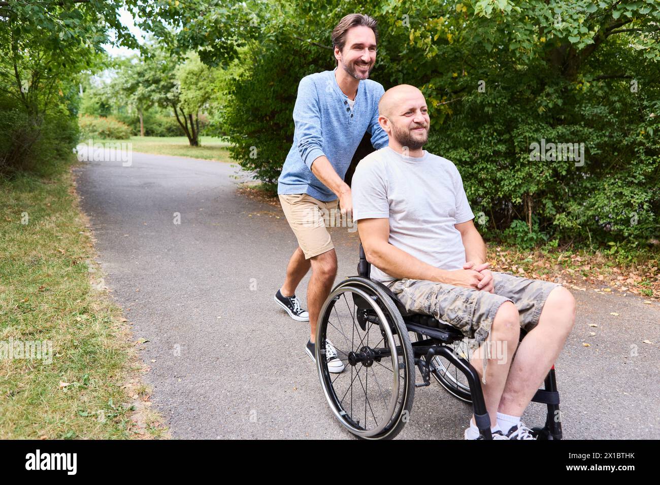 Ein fröhlicher Moment, in dem eine Person mit einem Rollstuhl und sein Freund an einem sonnigen Tag im Park lachen und Inklusion und Freundschaft hervorheben. Stockfoto