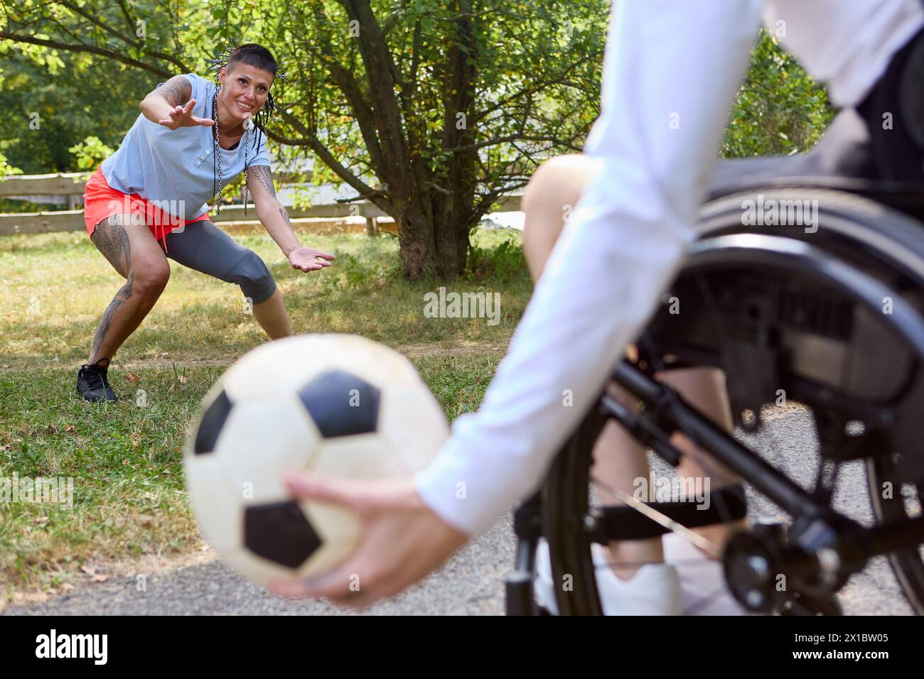 Eine fesselnde Szene, in der eine Person im Rollstuhl sitzt und Freunde im Freien Fußball spielen, die Freude, Inklusion und adaptive Sportarten zeigen. Stockfoto