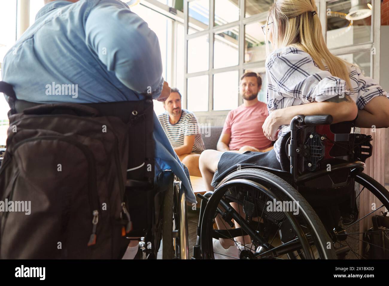 Eine Person, die einen Rollstuhl benutzt, führt in einem sonnigen cafÃ ein lebhaftes Gespräch mit Freunden. Das Bild zeigt Inklusion und soziale Interaktion zwischen d Stockfoto